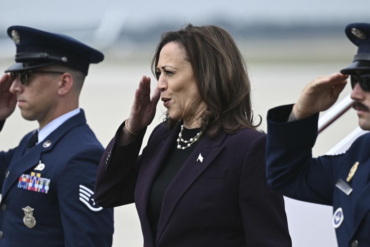 Kamala Harris salutes on a tarmac between two Air Force members in uniform