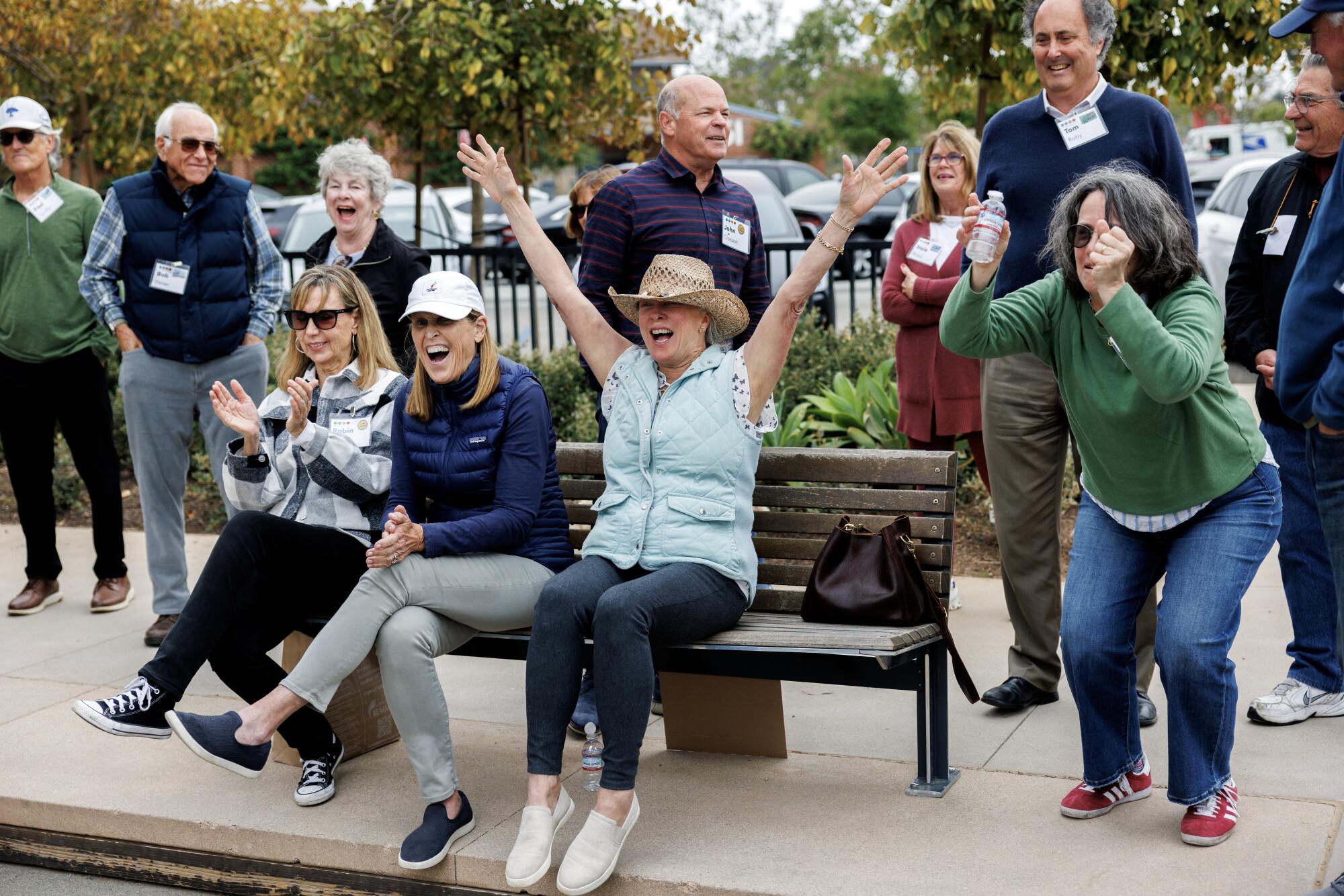 Three women cheering while sitting on a bench, another cheering next to them.