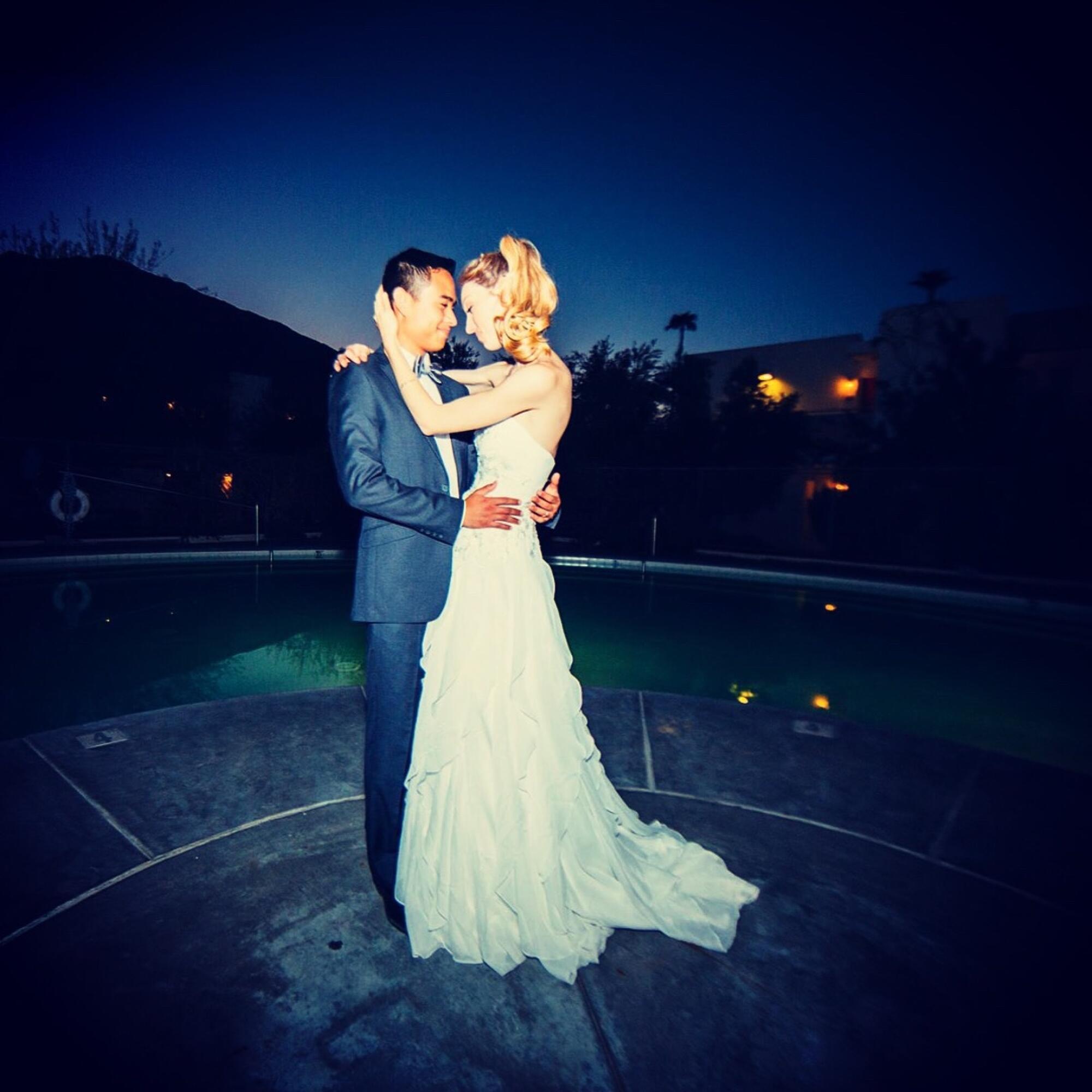 A bride and groom stand forehead to forehead, his arms around her waist, outdoors at twilight