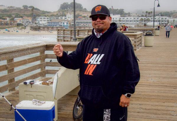 John Ramos holds a mackerel he caught fishing from the Pismo Beach pier in Southern California on July 18, 2024. (Travis Gillmore/The Epoch Times)