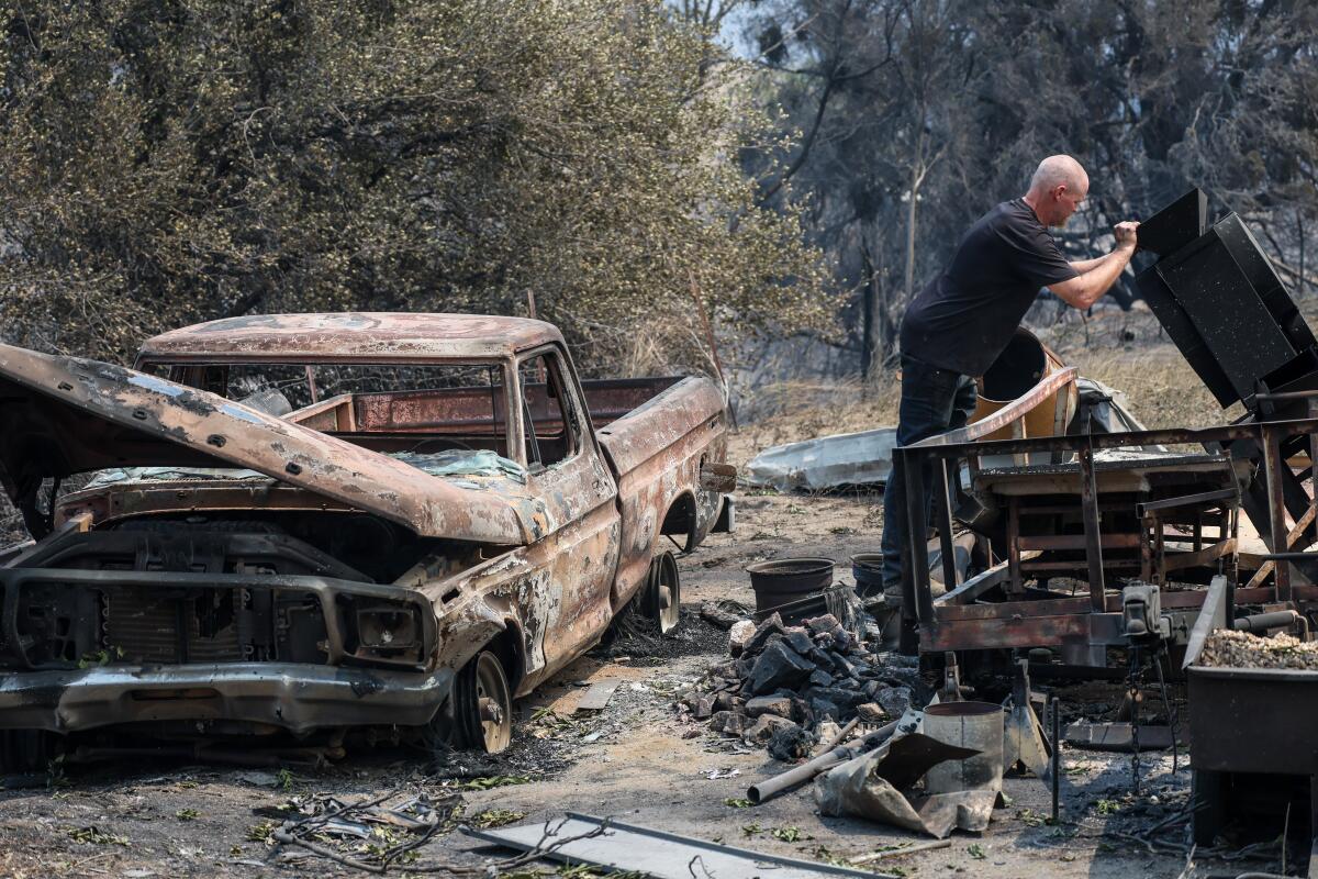 Sean Rains inspects his shaker table next to the rubble of his home and a burned pickup truck.