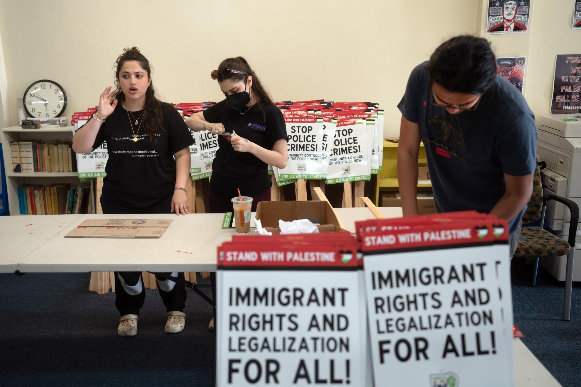 Two women and a man among protest signs and tables