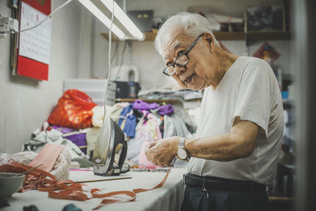 Master Yan wears a tailor’s thimble on a finger and has a “slobber line” in his mouth. The latter is an indispensable tool for properly stitching cheongsam and flower buttons. (Lau Wing-hong/The Epoch Times)