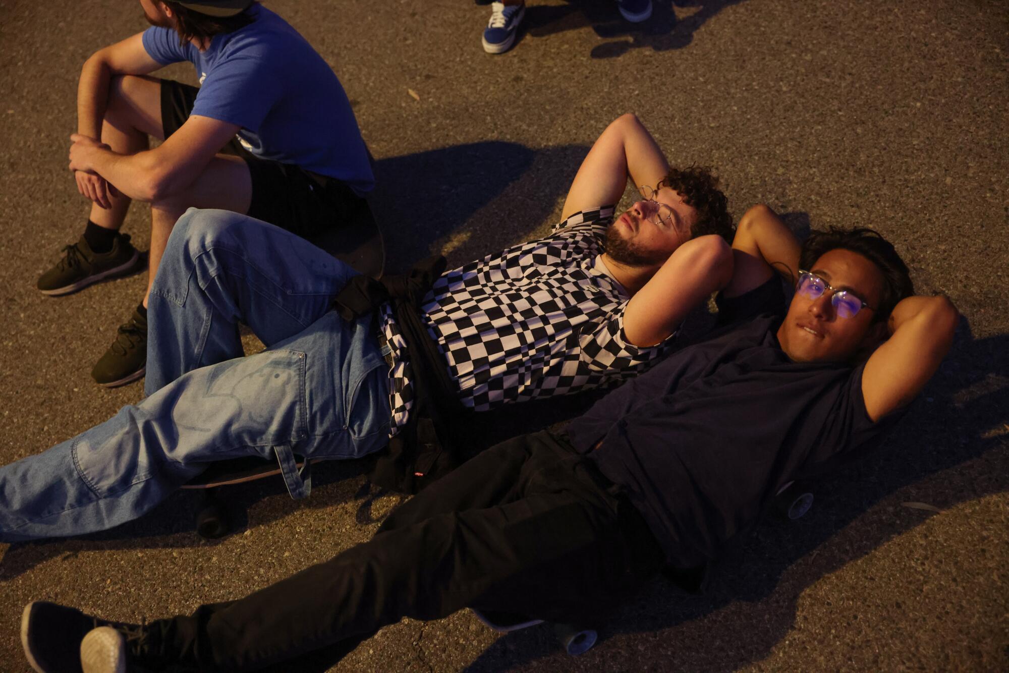 Two people lie on their longboards in the light of a streetlamp.