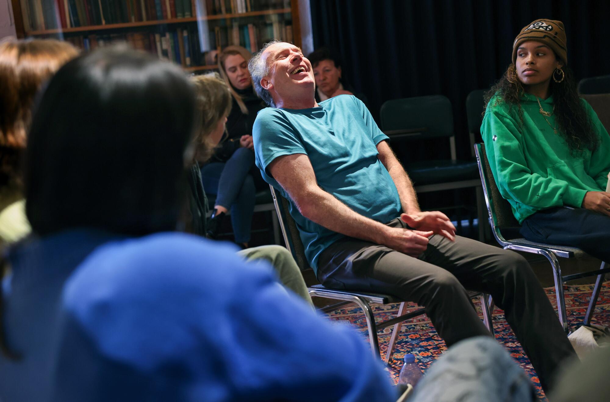 A man sitting in a discussion circle throws back his head and laughs