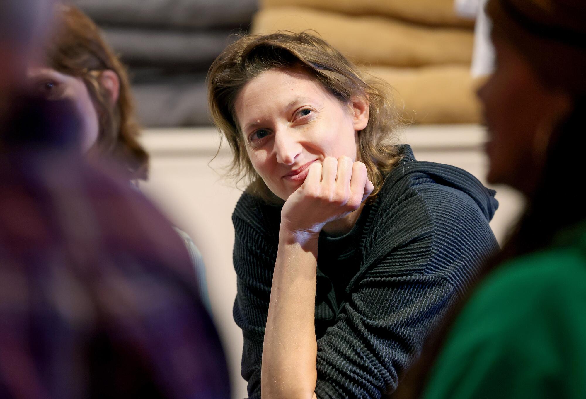 A person sits, head tilted and chin resting on hand, listening to another person speaking