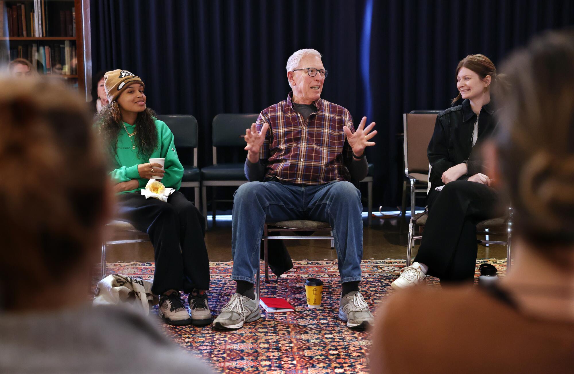 A seated man sits between two younger women in a circle, talking