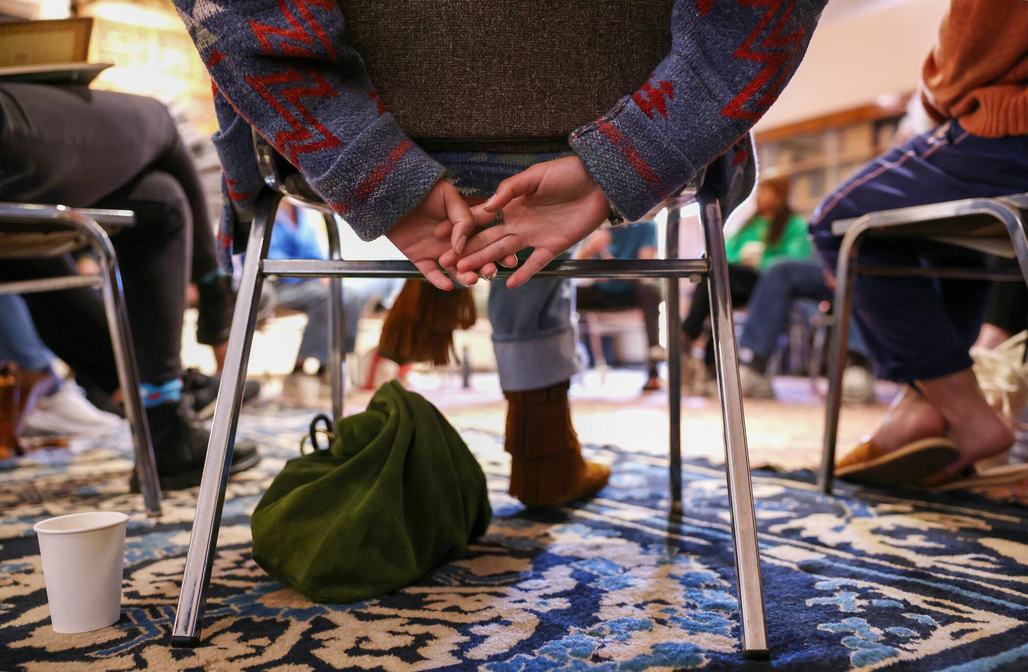 A closeup of a seated person's hands clasped behind them