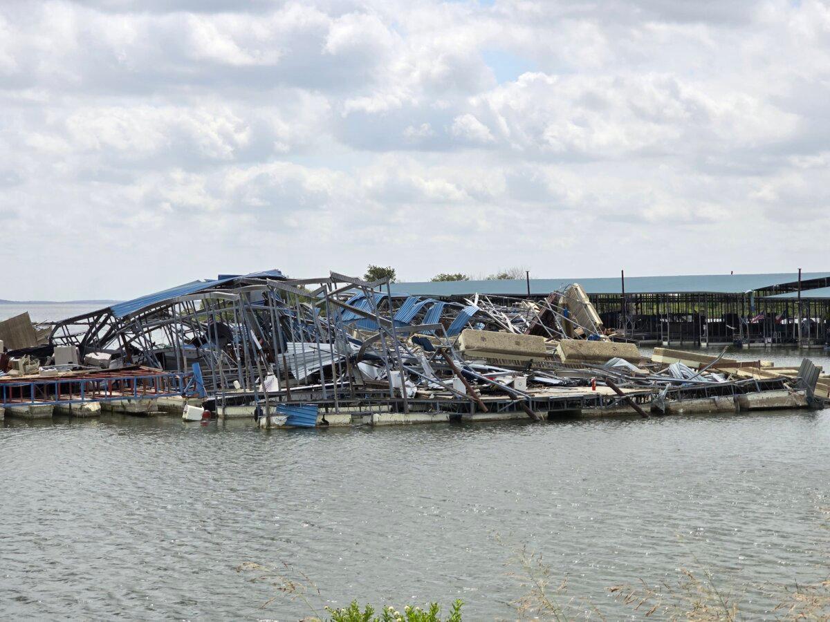 A wide-angle view of the debris pile where a powerful tornado plowed through Lake Ray Roberts Marina in Sanger, Tex., on May 25, 2024. Photos taken on July 29, 2024. (Below) Marina owner Bill Williams shows images of the damage to a trailer park at the marina. (Allan Stein/The Epoch Times)