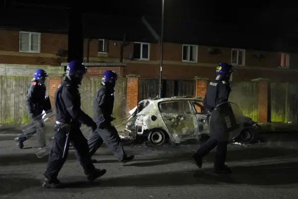 Police officers walk past a burnt out vehicle as they are deployed on the streets following a protest in Hartlepool, England, on July 31, 2024. (Owen Humphreys/PA)