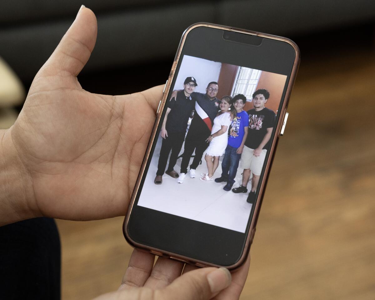 A photo displayed on a cellphone shows a man and a woman, flanked by three boys