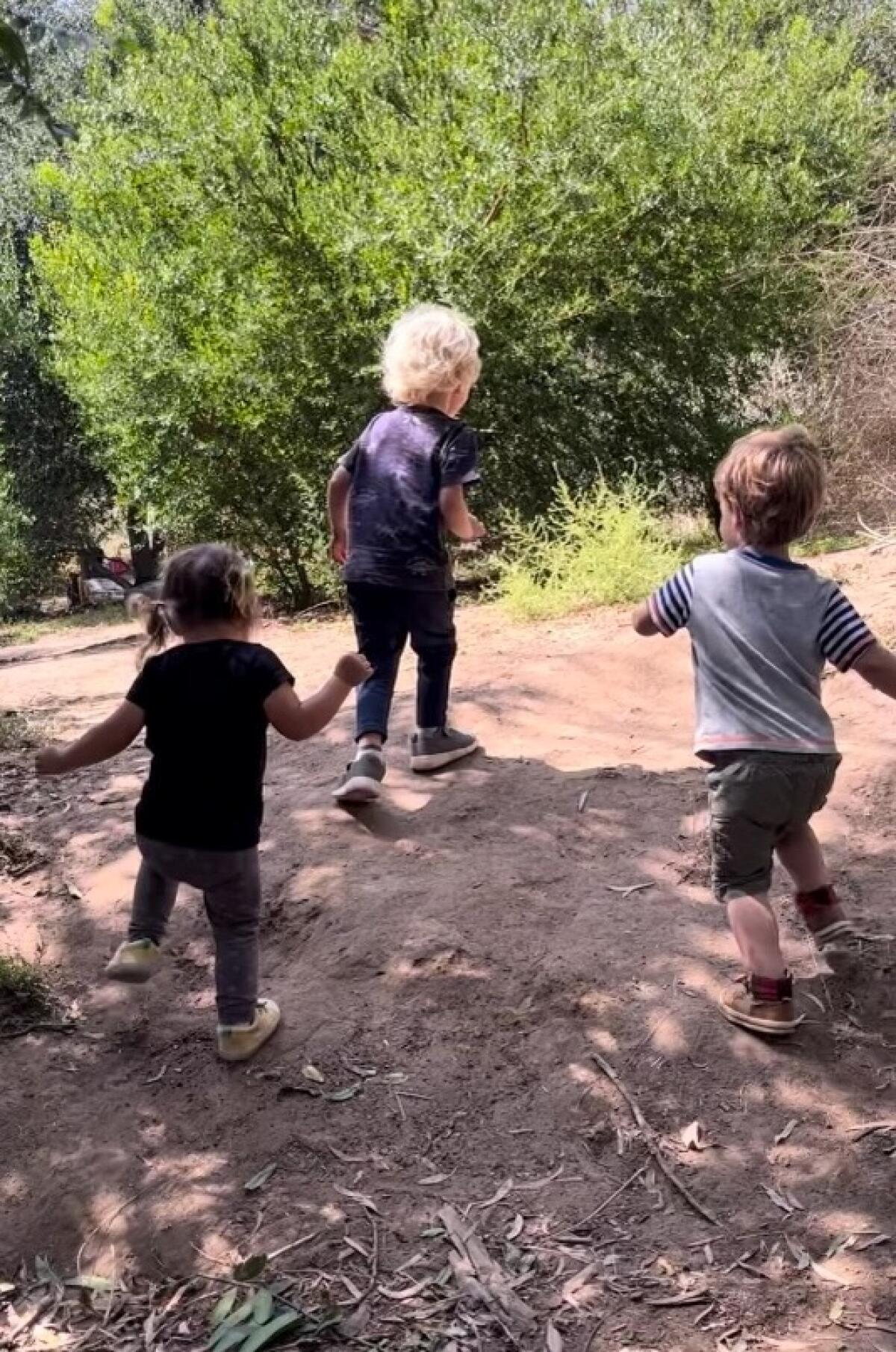 Three preschoolers racing up a path toward thick shrubs in the Childrens Garden in Elysian Park