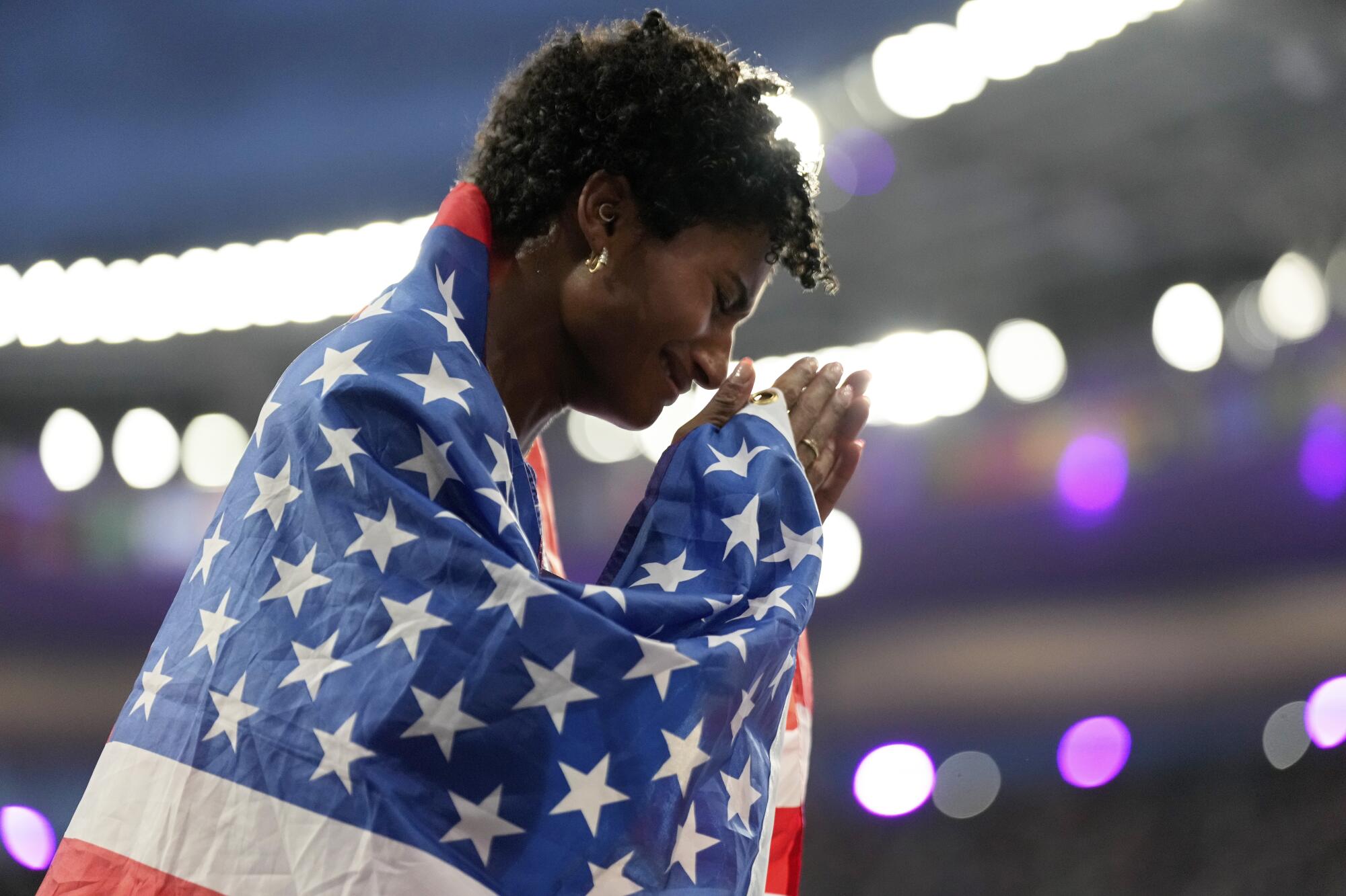 Anna Cockrell of the U.S. puts her hands together while wearing a U.S. flag under bright lights. 