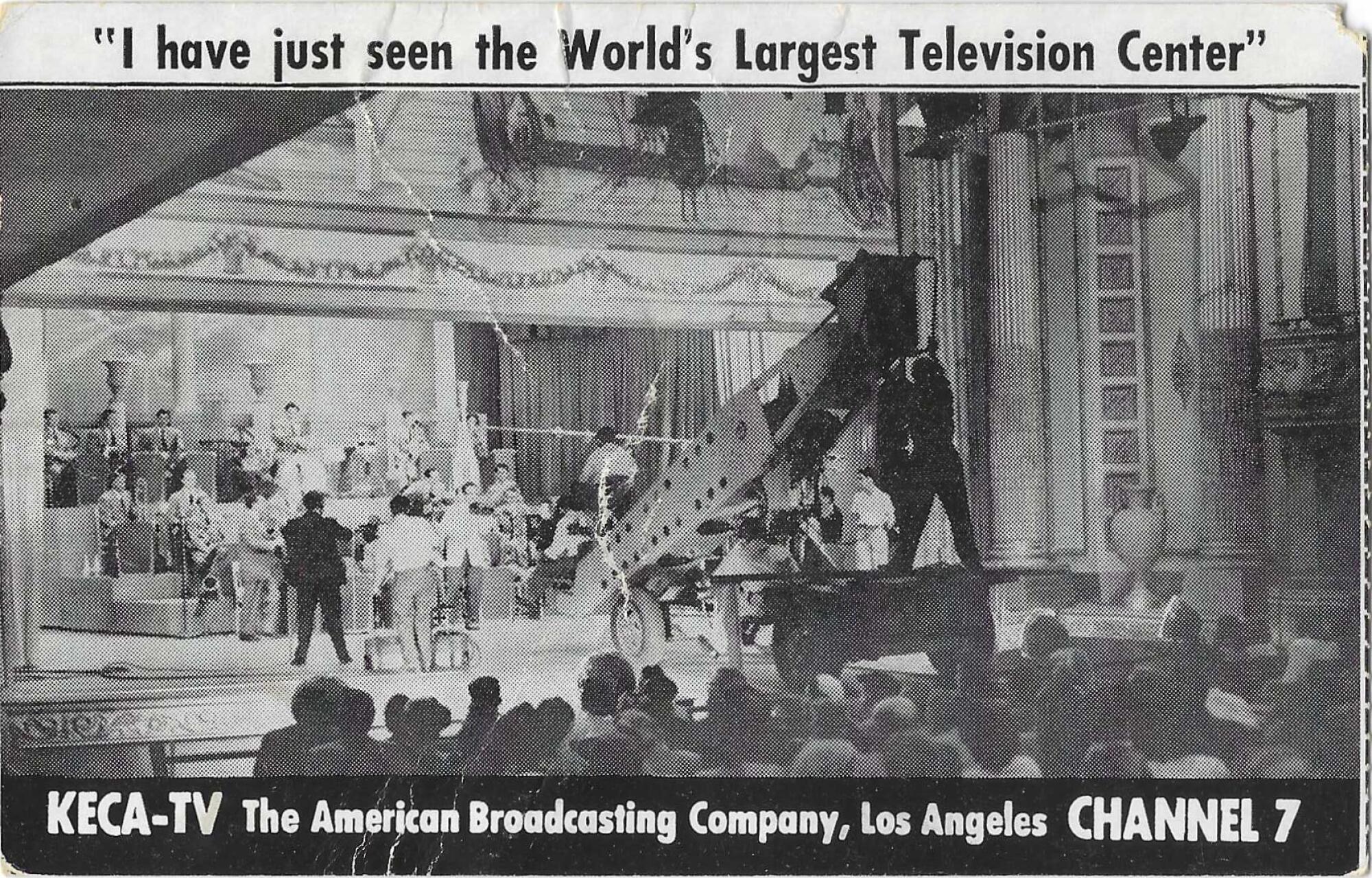 Black and white postcard of a large TV camera in a theater with a band on stage and and audience.