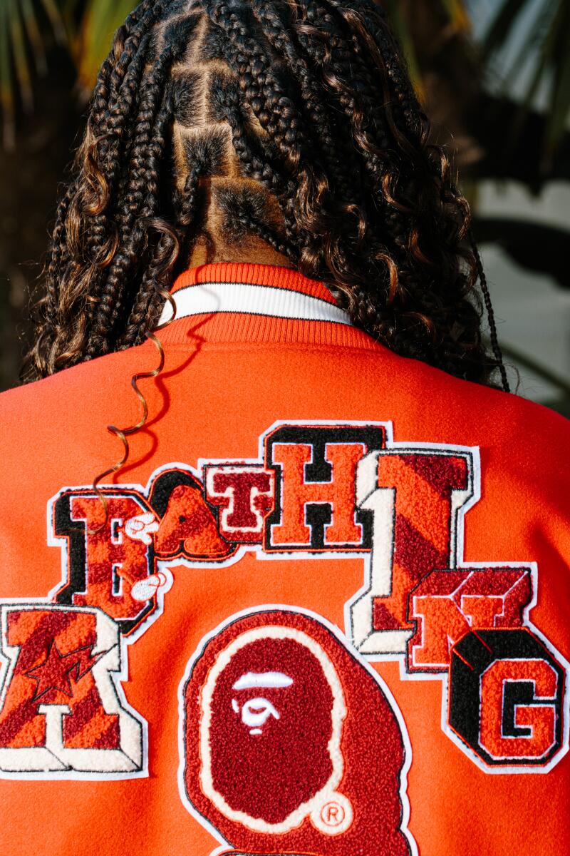 A detail of the back of a girl's head, showing her hair and a bright orange letterman jacket.