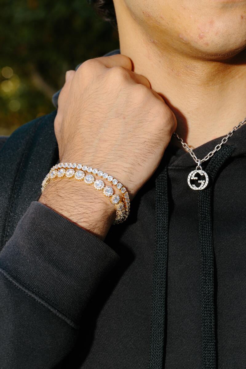 A closeup of a boy's wrist and neck, wearing a shiny bracelet and Gucci necklace.