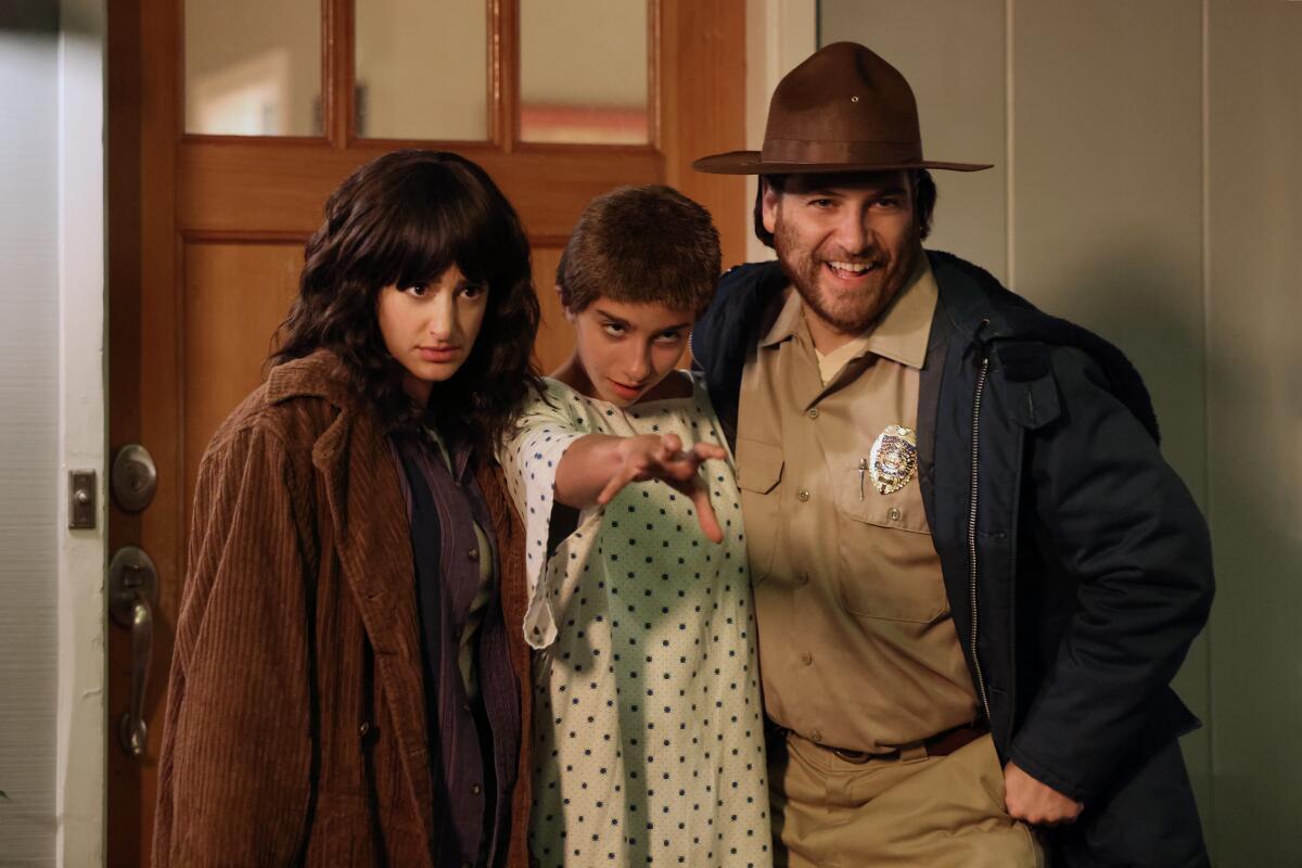 A woman, child and man in a sheriff's uniform stand pose for a photo in front of a doorway.