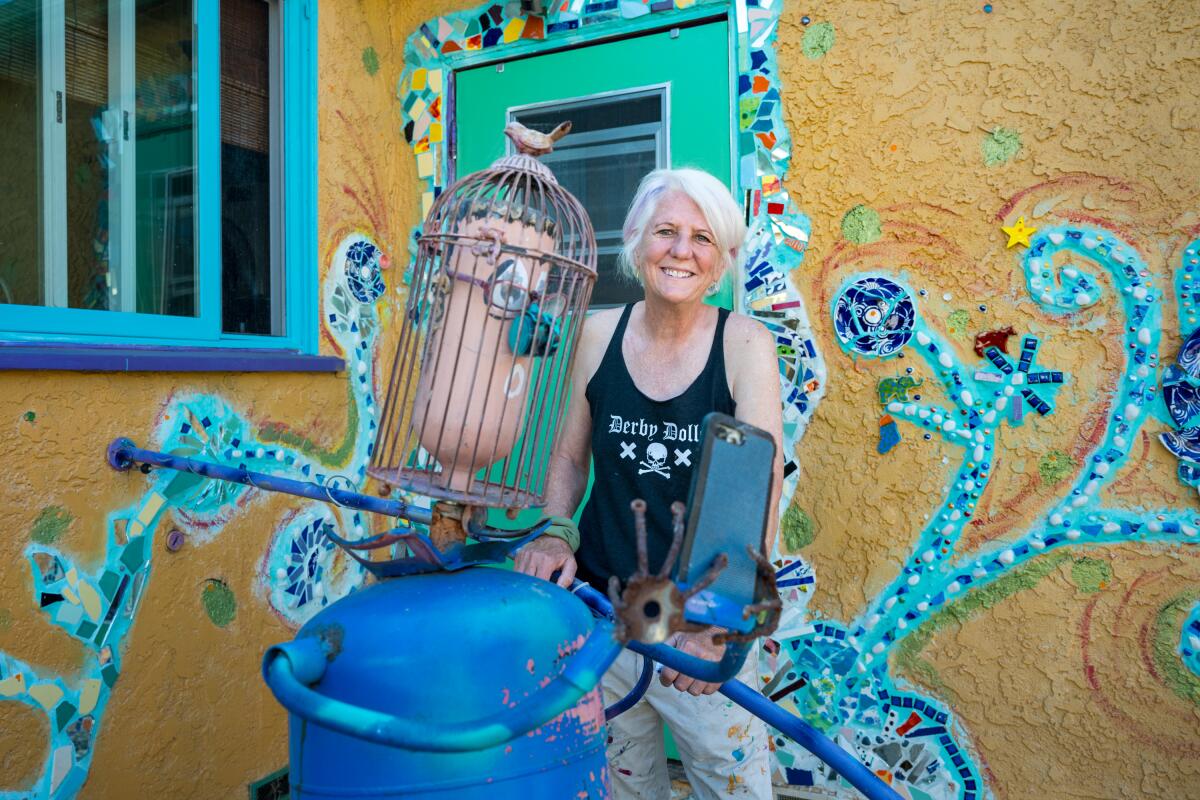 A woman behind a sculpture involving a bird cage in front of a decorated door and house 